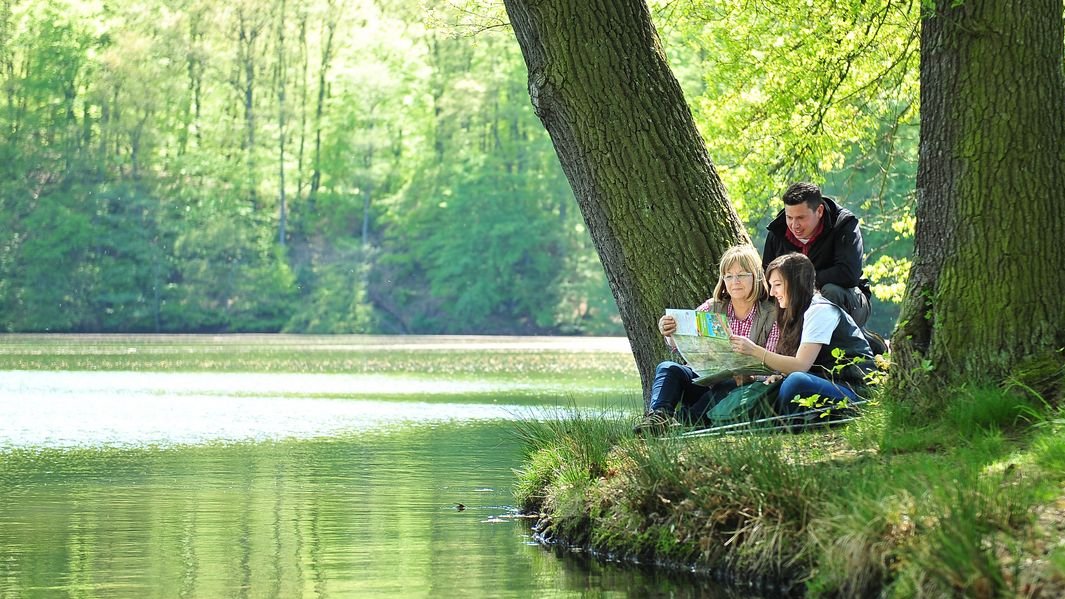 Familie schaut auf Karte am See in Thüringen